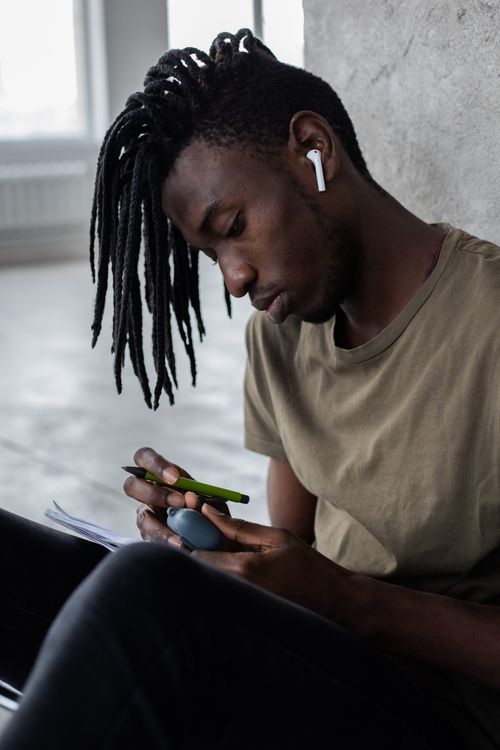 Free Serious African American male student closing case for wireless earbuds while doing homework assignment in notebook Stock Photo