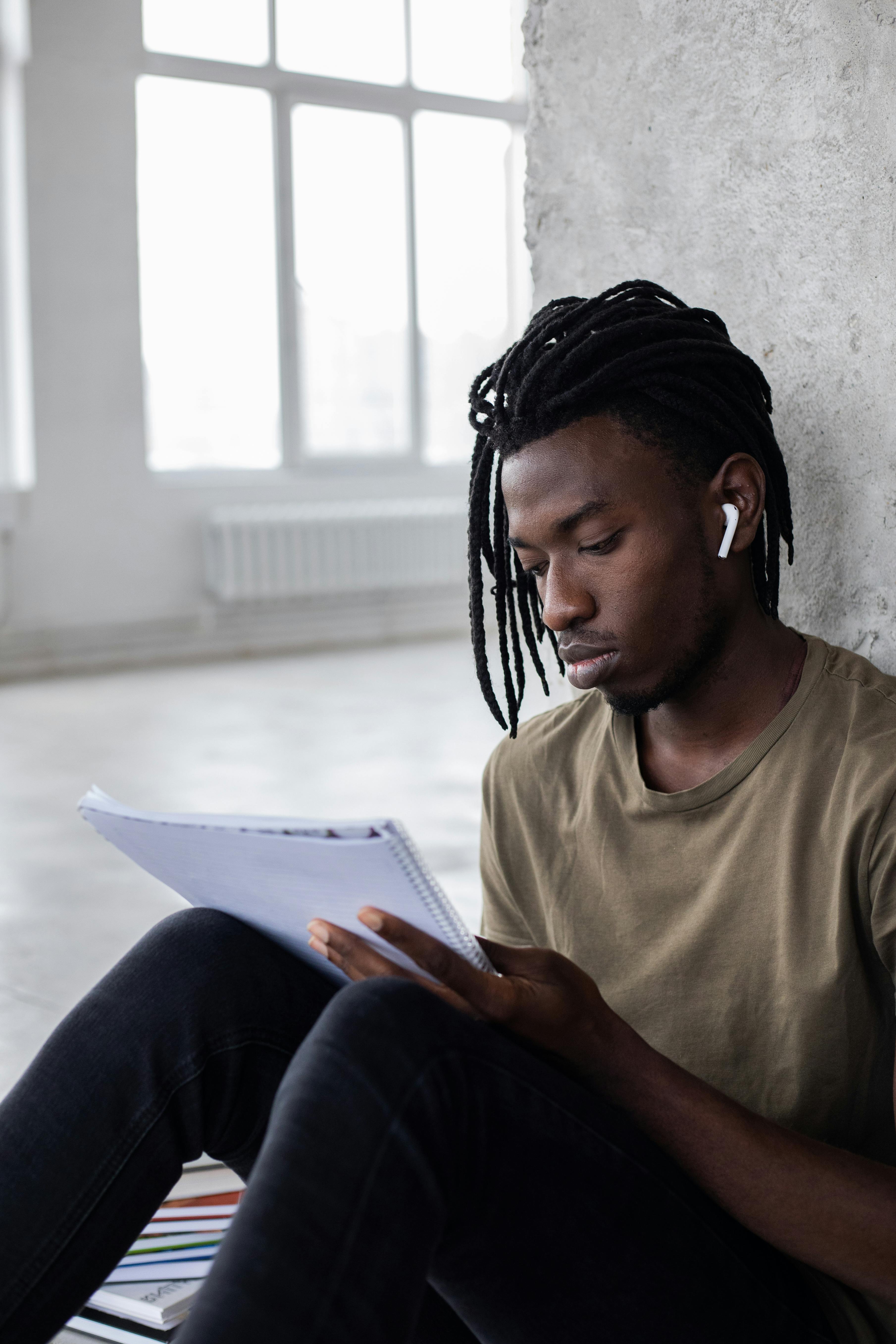 black man in earbuds reading notebook for studies