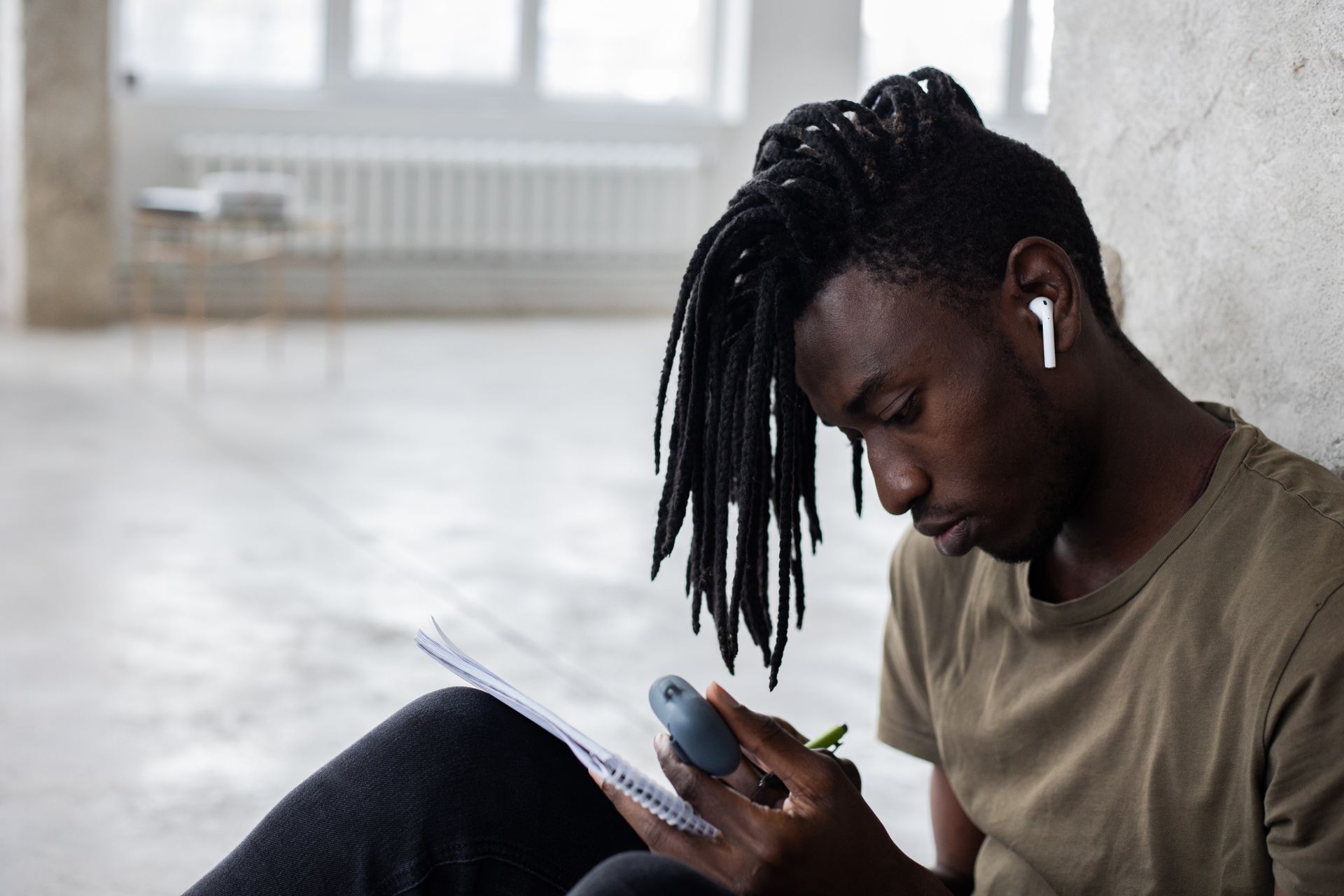 Focused black student in wireless earbuds writing in notebook