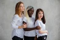 Multiethnic females wearing similar clothes standing close together showing support and unity standing against gray background