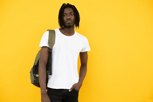 Serious African American male learner in casual outfit with hand in pocket standing against yellow background and looking away