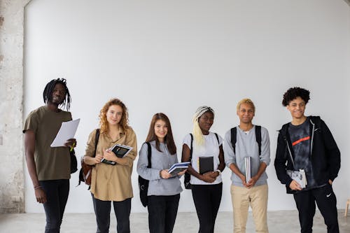 Group of diverse young multiracial classmates with notebooks and textbooks and backpacks smiling at camera