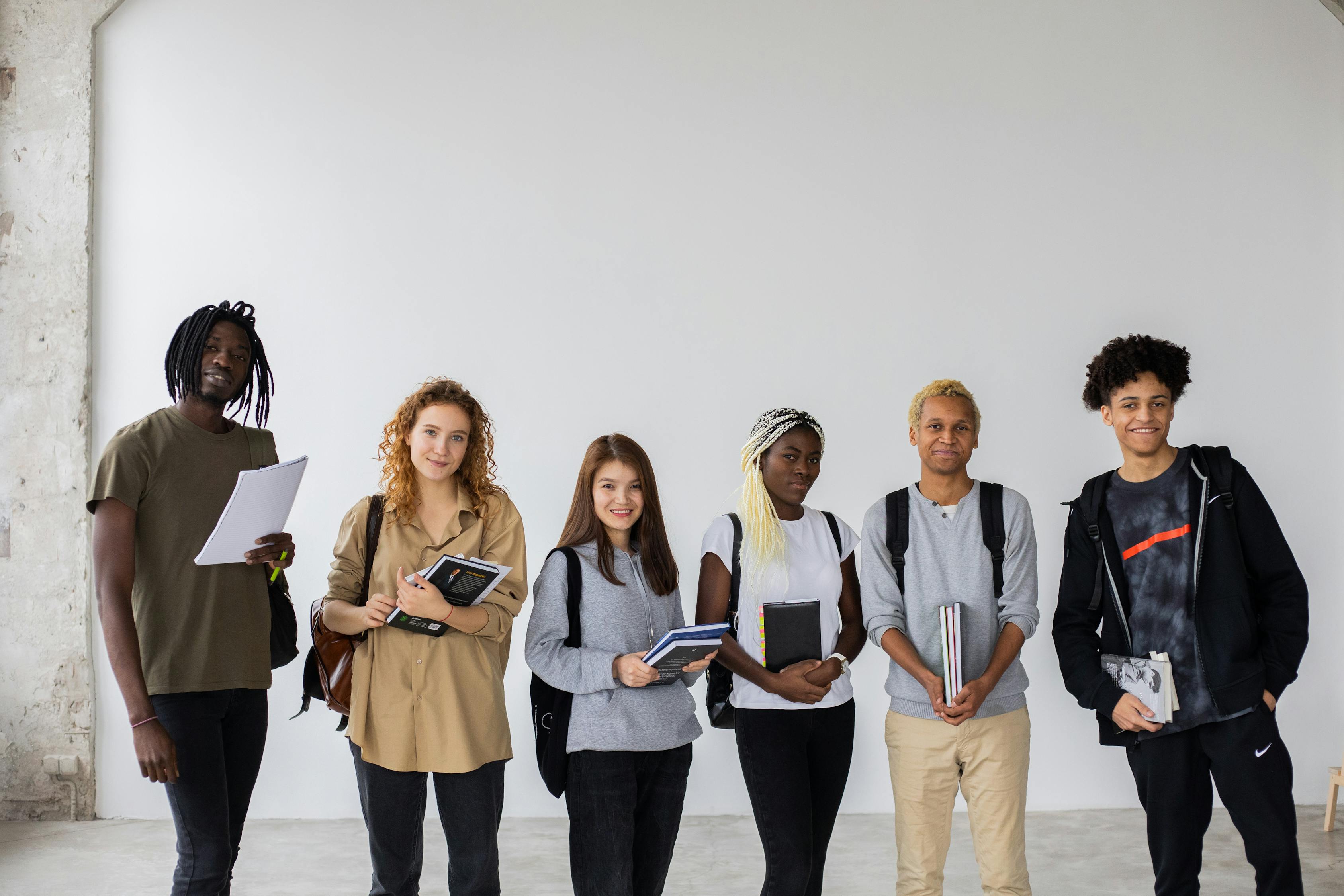 Group of diverse young multiracial classmates with notebooks and textbooks and backpacks smiling at camera