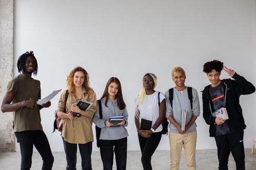 Free Group of smiling multiracial classmates standing with books and backpacks and smiling widely at camera Stock Photo