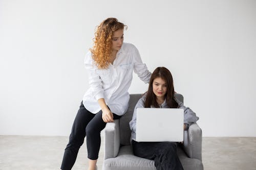 Serious women sitting on armchair and browsing netbook during teamwork in spacious empty room