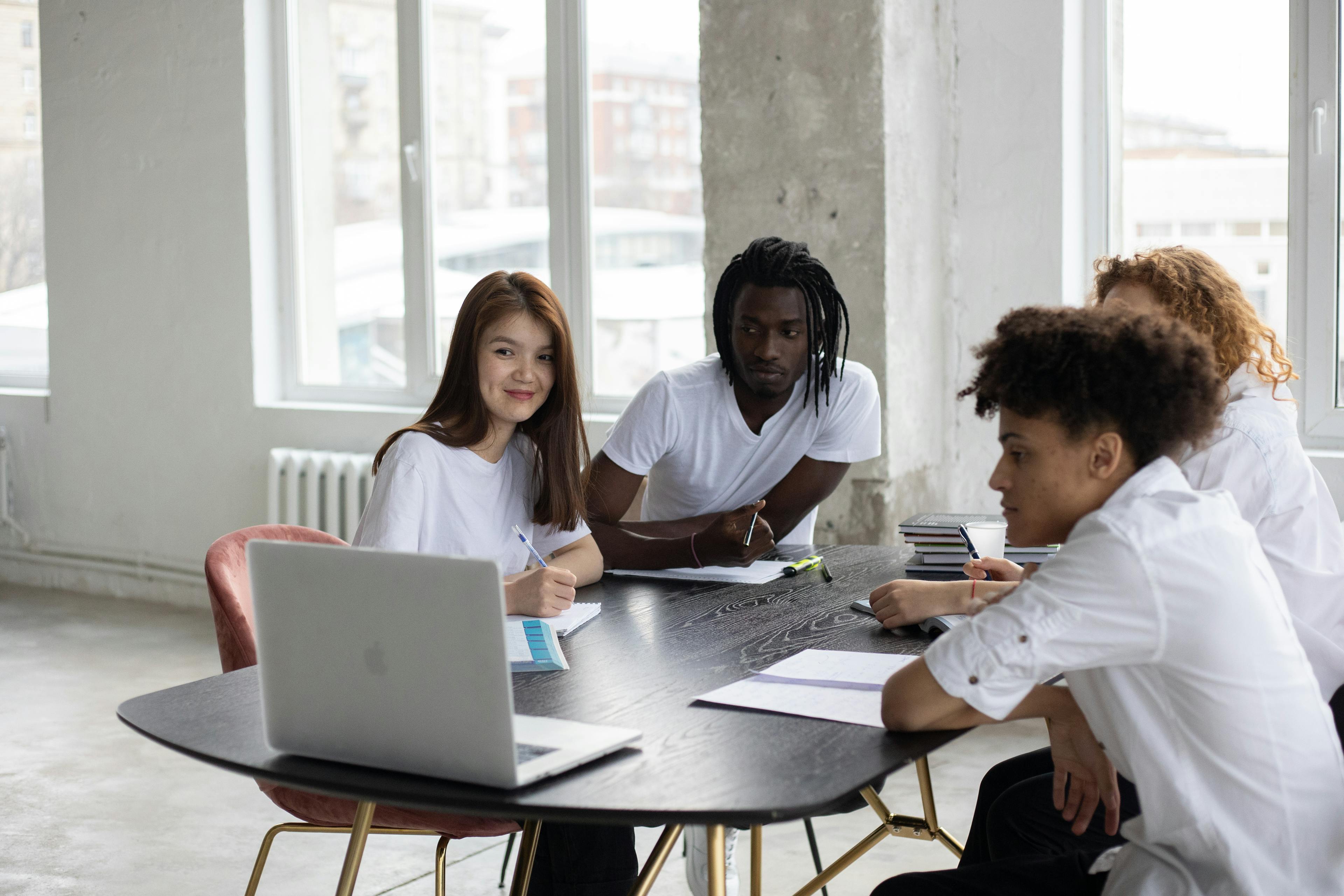 Group of diverse student sitting at table with copybooks and looking at screen of netbook during online studies in classroom