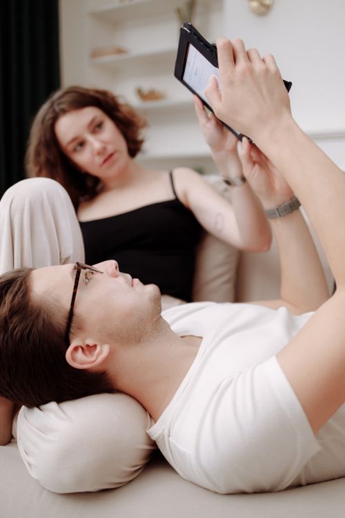 Free A couple enjoying leisure time indoors, browsing a tablet while relaxing together. Stock Photo