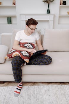 A young adult man shops online using a digital tablet in a cozy living room setting.