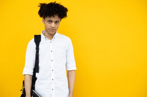 Unemotional black man with backpack standing on yellow background