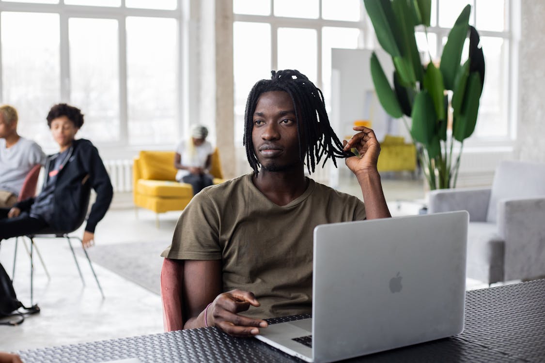 Free Pensive young African American male wearing casual t shirt working on contemporary netbook and looking away in deep thoughts while working in light loft coworking studio Stock Photo