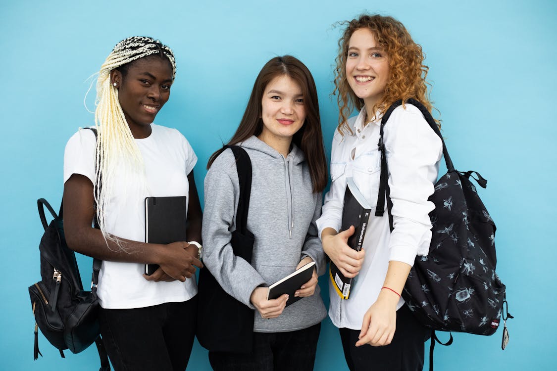 Free Happy multiethnic female students standing together on blue background Stock Photo