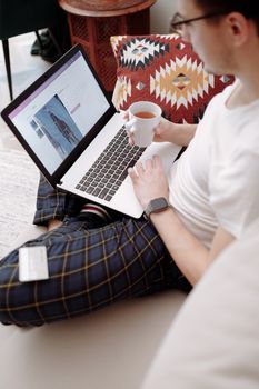 Man using laptop for online shopping while relaxing with a cup of tea at home.