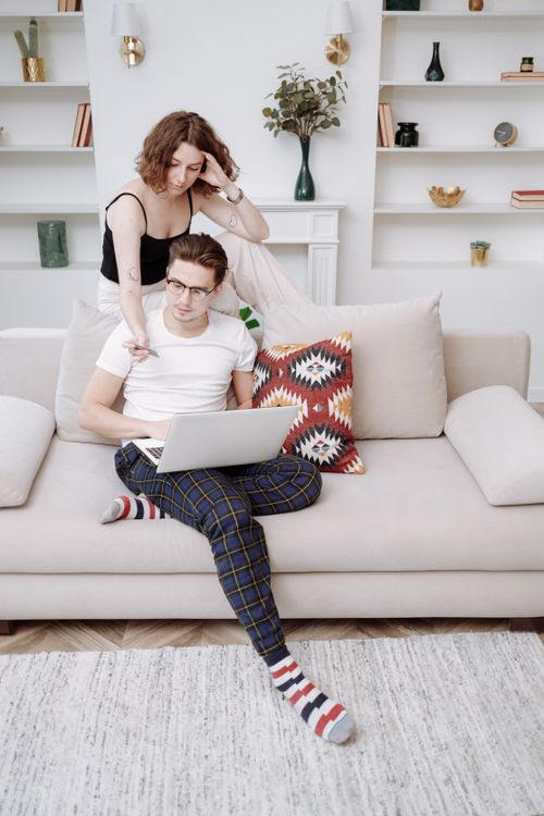 Free A young couple casually lounges on a sofa while browsing on a laptop at home. Stock Photo