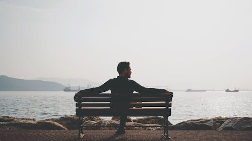 Man Sitting on Bench Near Body of Water