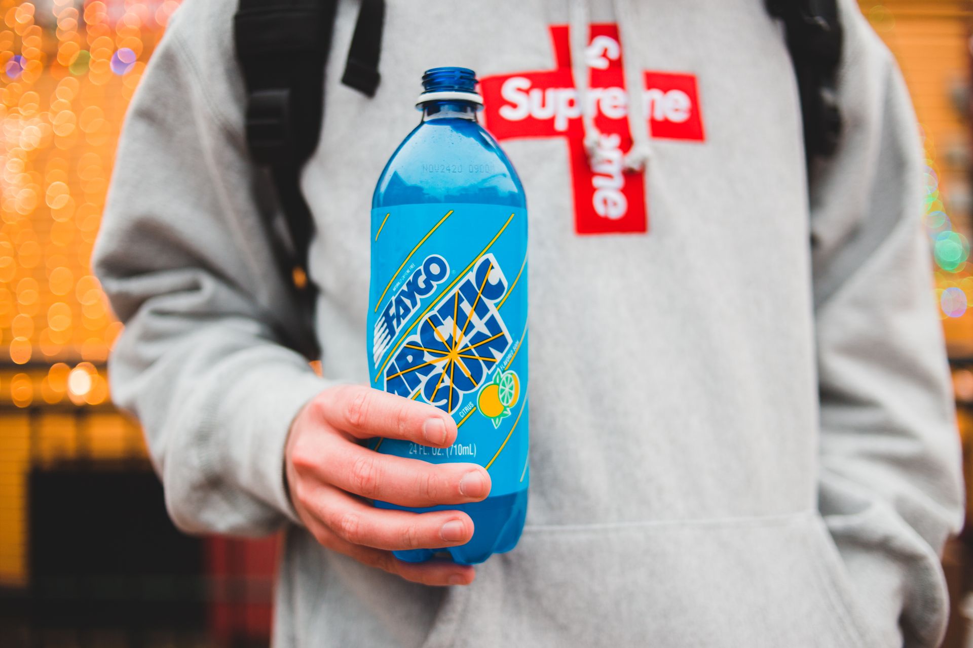 Crop unrecognizable male with hand in pocket and carbonated beverage with fruit and sun illustration on blue bottle