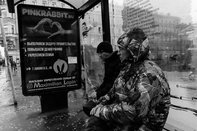 Unhappy Men Sitting On Bus Stop During Rain