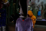 Back view of worker wearing velvet violet mascot costume and crop figure in bright clothes with tinsel on stilts and passers before glass case