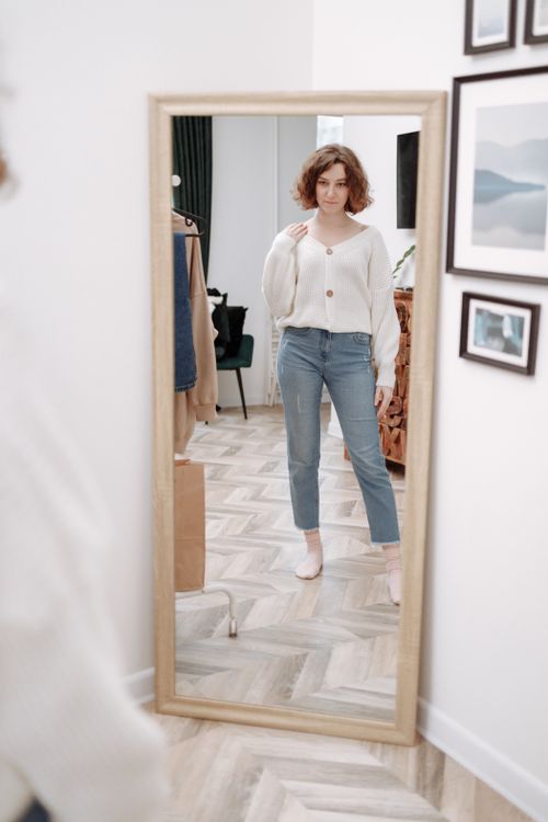 Free A fashionable woman admires her outfit in a full-length mirror. Bright and modern indoors setting. Stock Photo