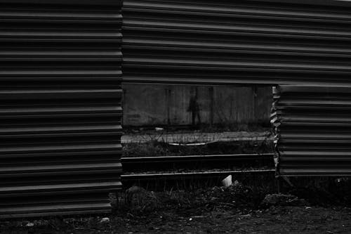 Black and white of automobile road and rails visible through square hole in lower part of enclosure from metallic profile