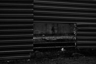 Black and white of automobile road and rails visible through square hole in lower part of enclosure from metallic profile