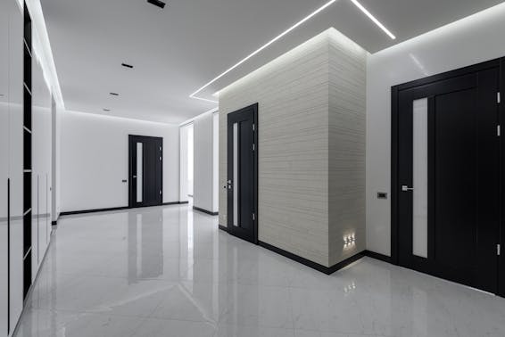 Modern spacious corridor with white walls and floor and black doors and ceiling decorated with LED lights