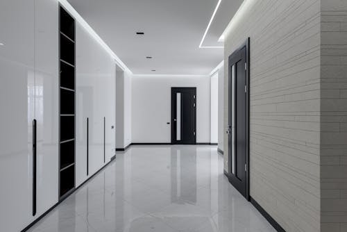 Wide corridor in modern house with white tiled walls and floor black wooden doors and shelves for storage built in wall