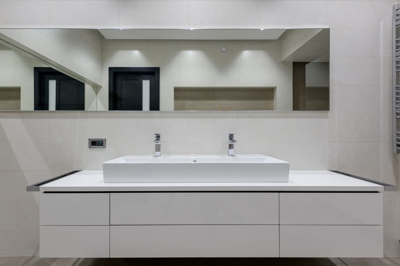 Modern gray-tiled bathroom with a floating white vanity, illuminated mirror, glass shower, wall-hung toilet, and plant decor.