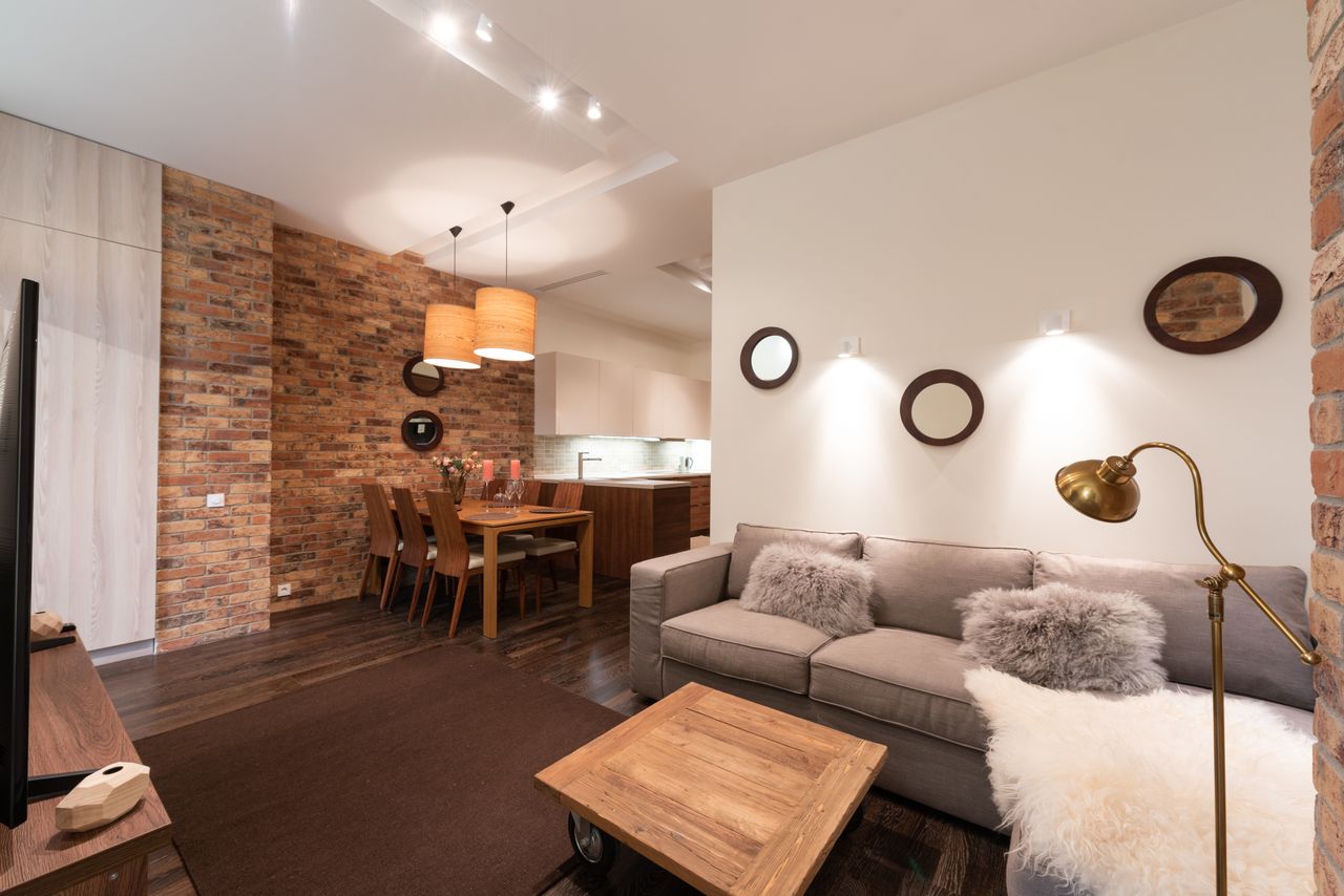 Open-plan brick loft with kitchen, dining table, and gray sofa