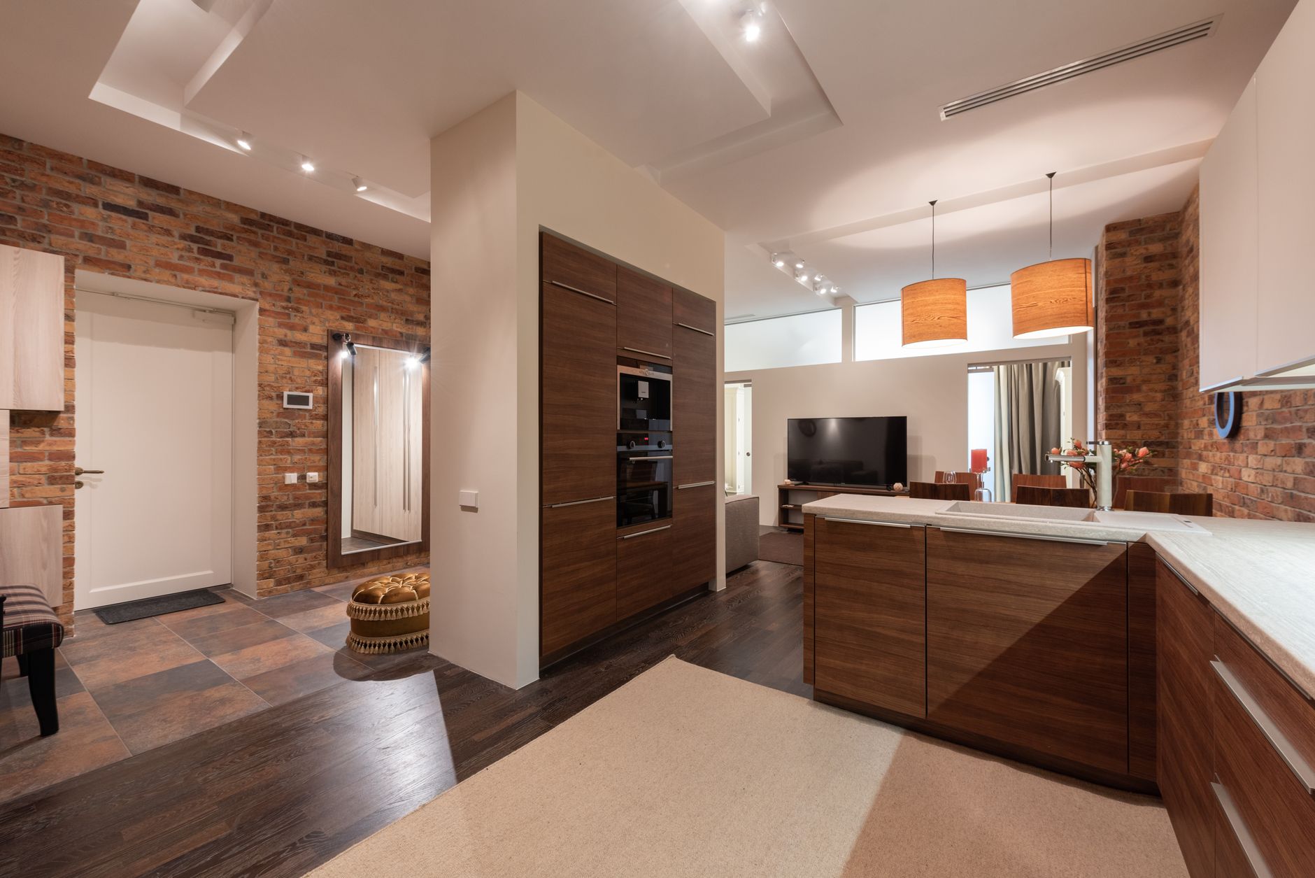 Interior of modern light studio with cabinets and door near TV and lamps hanging on ceiling and mirror near windows with curtains and oven with microwave near dining zone