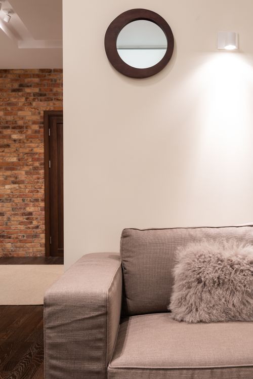 Free Interior of light modern apartment with gray couch with soft pillows near mirror on white wall near door with brick wall Stock Photo
