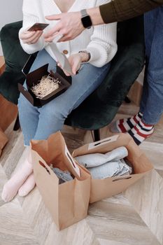 Couple unpacks paper shopping bags with clothes and gifts. Cozy indoor setting.