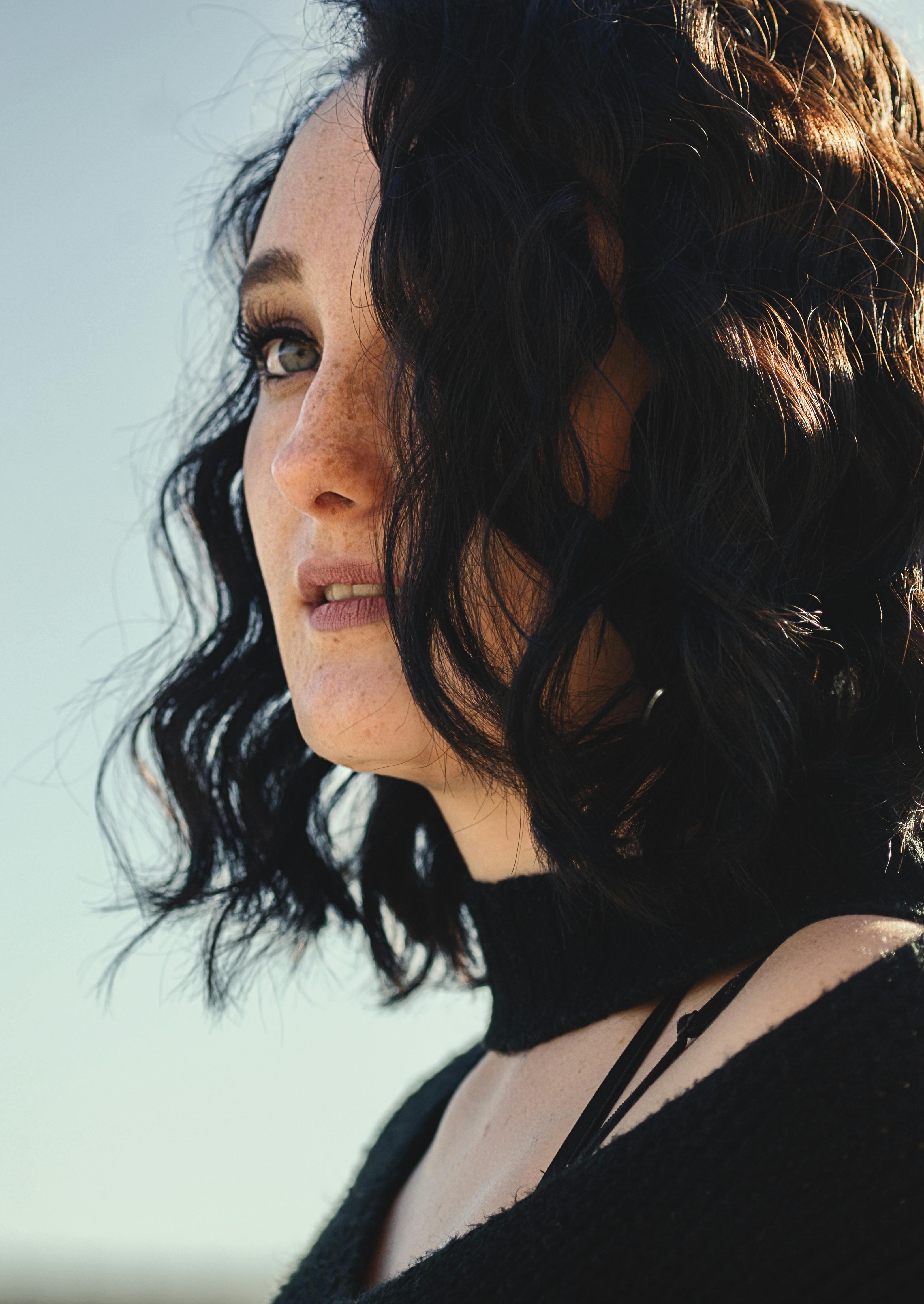 Close-up of a woman with curly short hair outdoors in sunlight.