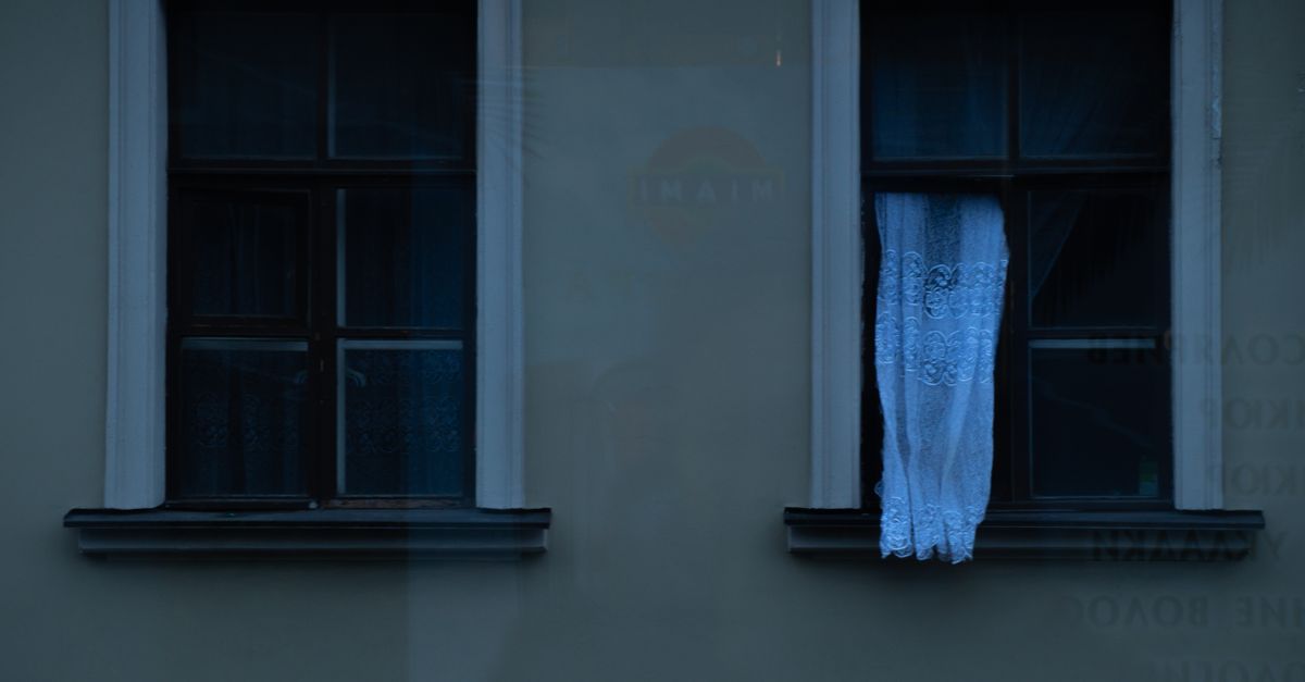 Fachada escura com janelas vintage e cortinas de renda ao crepúsculo, evocando tranquilidade.