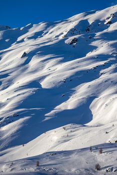 Snowy mountain landscape in Livigno, Lombardy, Italy, under a clear blue sky.