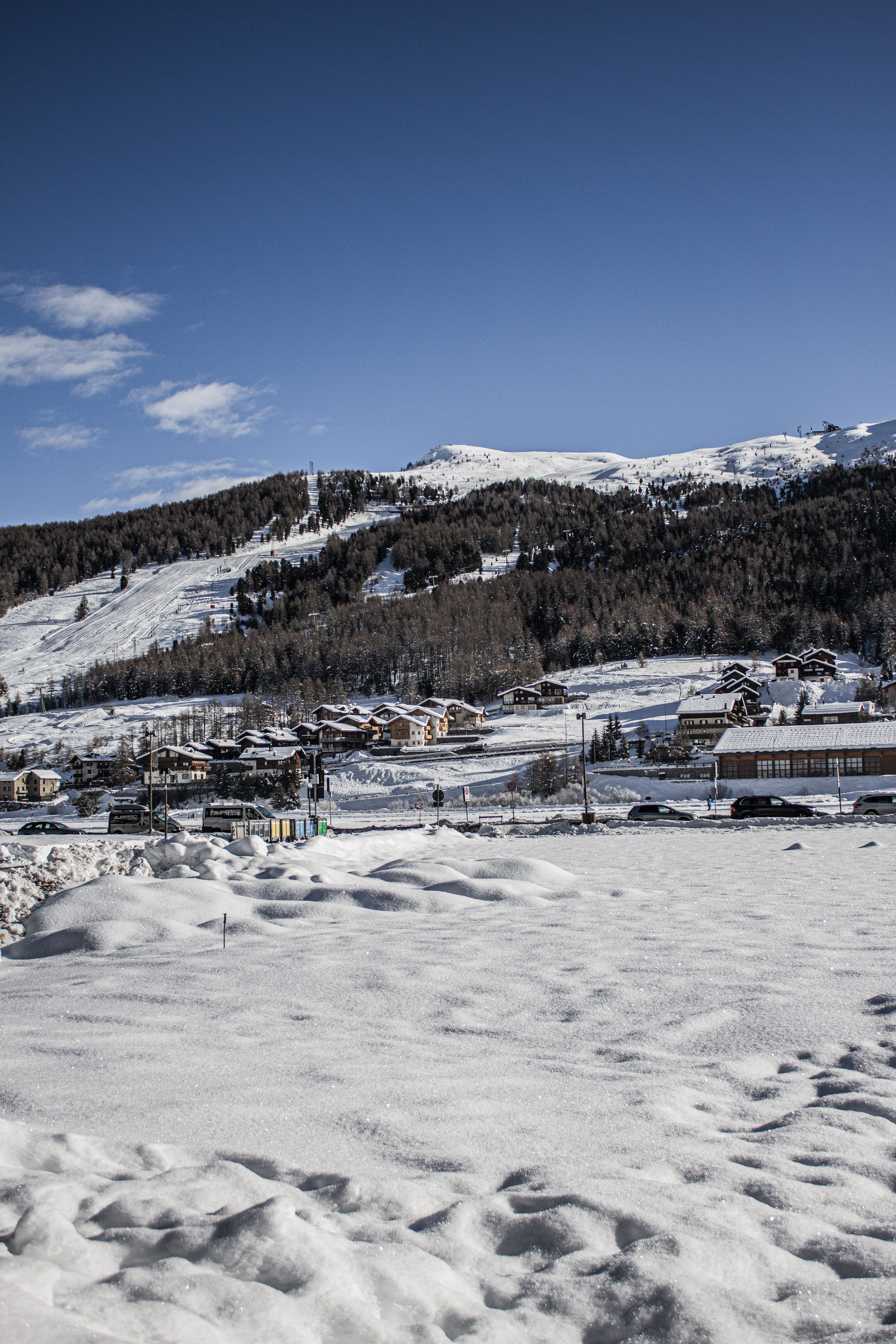 A picturesque snow-covered town in Livigno, Italy, with mountainous backdrop under a clear blue sky.