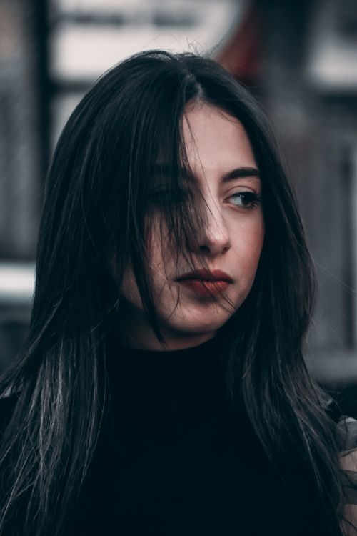 Free Close-up portrait of a woman with long black hair, wearing a turtleneck, looking afar in an outdoor setting. Stock Photo