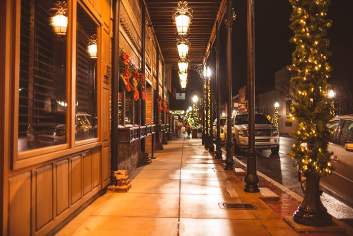 Shopping center storefronts and walkway decorated with Christmas wreaths and lights at night
