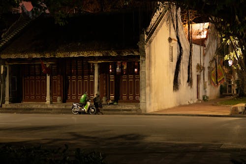 A Person Sitting on a Parked Motorcycle while Talking to Another Person Sitting on the Concrete Stairs Outside the House