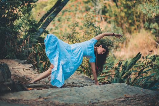 Full body of barefoot female in dress doing lateral bend supported by leg and arm in nature during yoga session