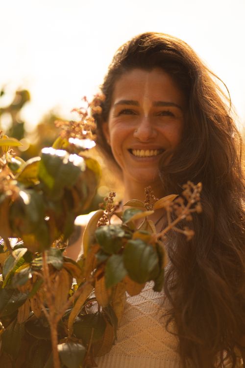 Free Happy female with long hair and pattern on face standing near branch with green leaves in sunlight and looking at camera Stock Photo