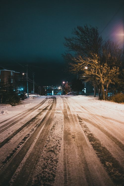Free Empty roadway with traces between streetlamps and trees under dark sky in winter city Stock Photo