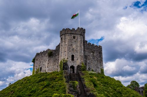 Free Majestic Cardiff Castle in Wales, topped by a flag, under dramatic cloudy skies. Stock Photo