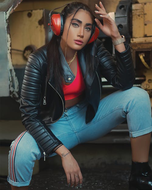 Woman in Black Leather Jacket and Blue Denim Jeans Wearing Headphones while Posing at the Camera