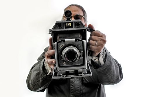 Free A man holding a vintage camera, capturing the essence of traditional photography on a white background. Stock Photo