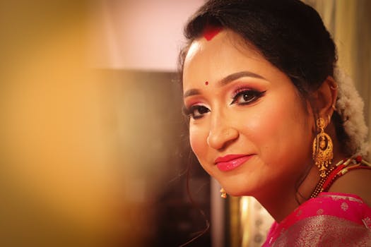 A close-up portrait of a smiling Indian woman in traditional makeup and jewelry with a warm background.