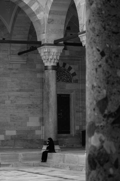 Free Black and white image of a woman in Istanbul mosque courtyard, showcasing Ottoman architecture. Stock Photo