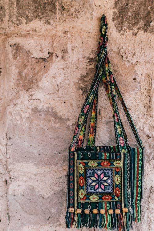 Bright knitted bags in ethnic style with embroidery pattern hanging on shabby wall