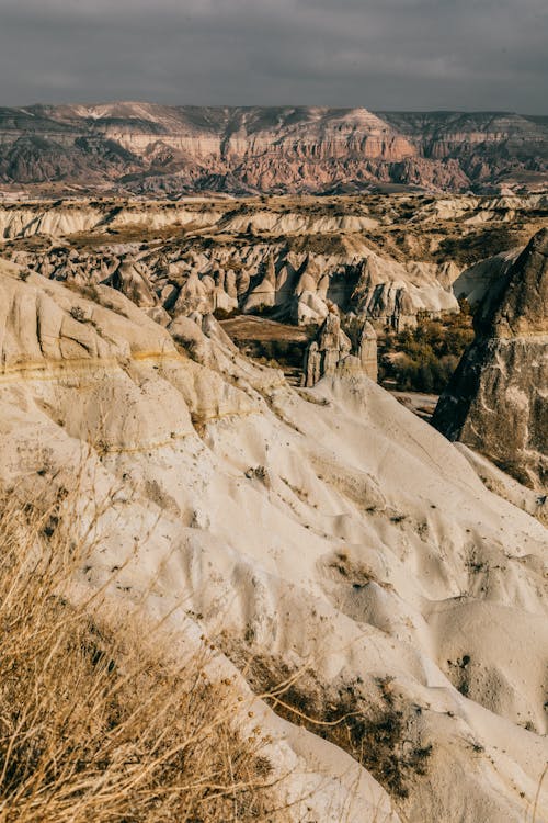 Spectacular landscape of dry uneven mountains with sand and grass in valley in summer day under gray cloudy sky