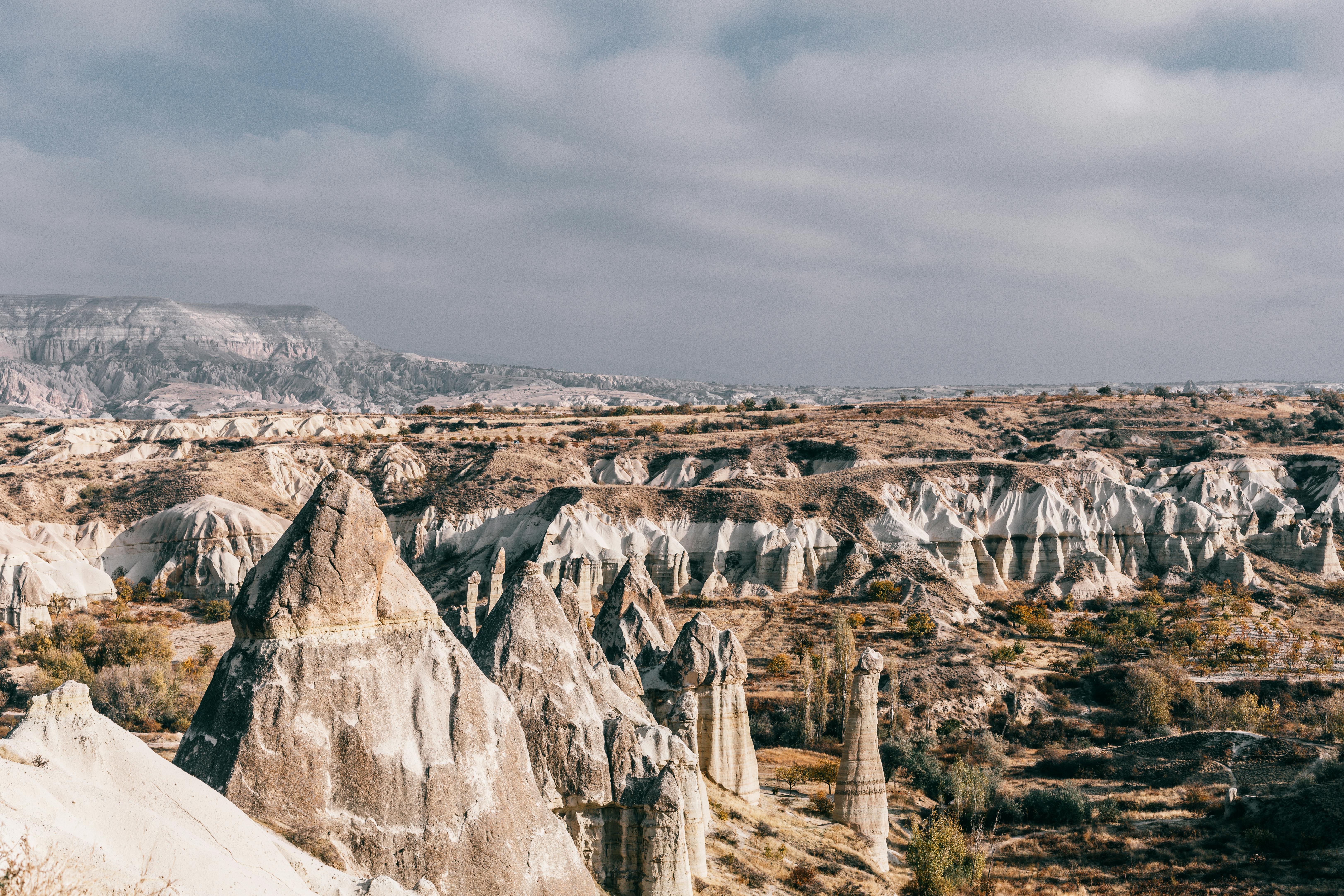Free Breathtaking landscape of dry rocky formations near uneven mountains in valley with plants and bushes in Turkey in Cappadocia region in summer day under gray cloudy sky Stock Photo