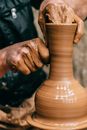 Crop anonymous craftsman doing clay modeling while making vase on pottery wheel on blurred background
